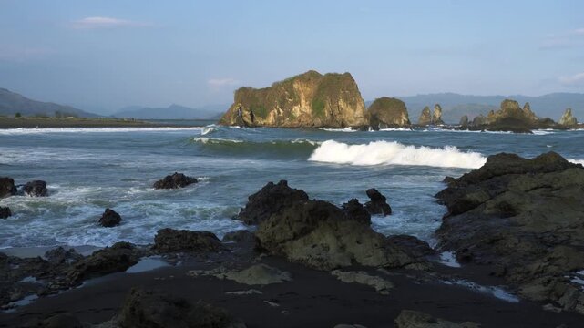Love Bay - Teluk Love in Jember east java. A scenic view of a rocky cliff surrounded by ocean waves crashing under a blue sky. The intricate rock formations and the dynamic movement of the waves