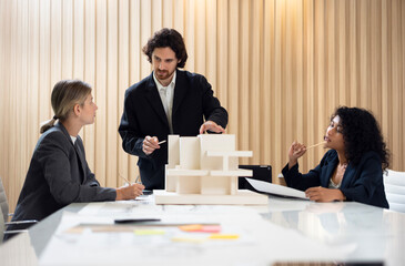 Businessman leading a meeting and presenting a housing project plan using a scale model to his colleagues in a modern office