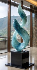 Abstract sculpture of swirling teal and light blue glass, placed on a black pedestal.  Large, modern art piece with a flowing, dynamic design against a background of panoramic views