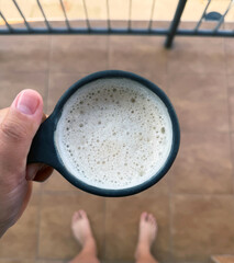 A cup of coffee with milk foam, held in her hand, bare feet.