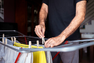 
Unrecognizable person hanging clothes with clothespins inside the house.
Man doing housework at home