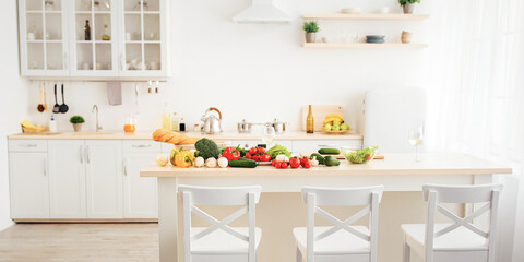 Food blogger workplace, vegetarianism and home health care during COVID-19 outbreak. Kitchen interior with bright fresh vegetables and white wine in glass on white furniture, free space, nobody