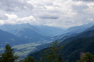 Wide valley view with layered mountain ranges, cloudy sky, villages and fields in the distance, panoramic alpine landscape