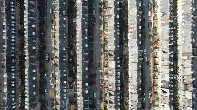 Aerial top-down view of tightly packed terraced houses in a residential neighborhood with parked cars and narrow streets. Urban cityscape captured in sunlight, showcasing symmetry and dense housing ar