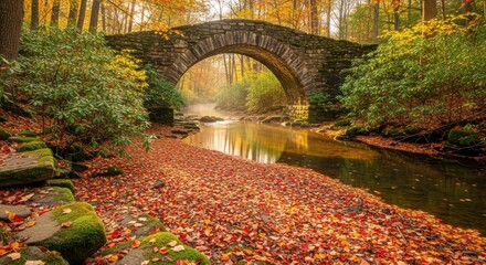 Photo of an old stone arch bridge crosses a gentle stream in a forest during autumn, with fallen leaves covering the ground and colorful foliage creating a picturesque and serene landscape