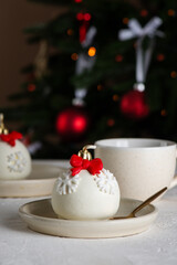 Christmas ball cakes with red bows and snowflakes with cup of tea on a table with a Christmas tree in the background. Vertical orientation.