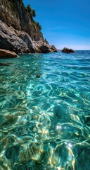 Fototapeta premium Crystal-clear turquoise water lapping against a rocky shoreline, with lush greenery on the cliffside, under a vibrant blue sky
