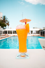 Cóctel tropical de color naranja con sombrilla decorativa servido junto a piscina en ambiente vacacional