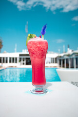 Cóctel rosa con espuma y decoración colorida servido en vaso alto frente a piscina de resort