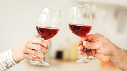 Romantic couple enjoying dinner at home, love, relationship and love concept. Happy couple celebrating and holding glasses of red wine in modern kitchen interior, close up, copy space, cropped