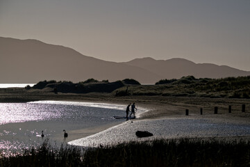 Summer evening silhouette of people at the seaside with hills in the background