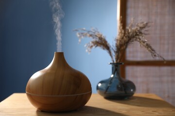 Modern aroma lamp and dry plants in vase on wooden table indoors, closeup