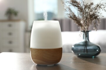 Modern aroma lamp and dry plants in vase on wooden table indoors
