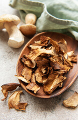 Dried porcini mushrooms resting in wooden bowl on gray textured background
