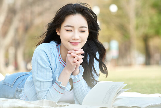 Young adult female relaxing on grass reading a book outdoors in spring park