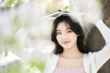 Young woman holding a book above her head under cherry blossom trees in spring