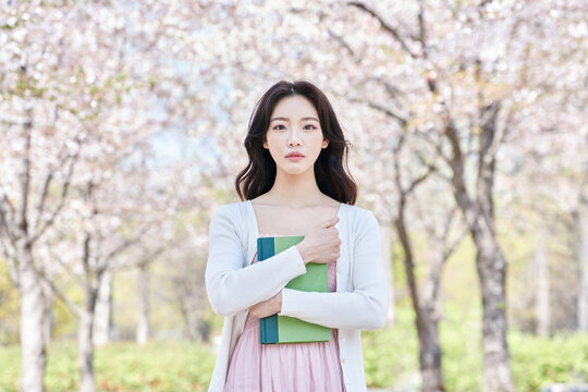Young Asian female student holding a green book outdoors in spring park