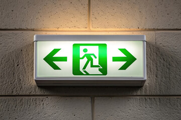 Illuminated Emergency Exit Sign on Textured Wall Guiding Evacuation Route with Arrows and Running Figure, a Vital Safety Measure with Low Feedback