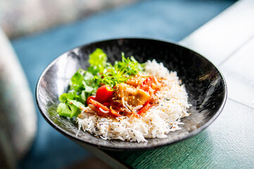 Black bowl with white rice, topped with roasted vegetables, cilantro, microgreens, and sesame seeds. Vibrant, fresh, and appetizing food presentation