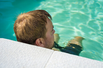 Man relaxing in a swimming pool in blue water on a sunny day in a private backyard pool, concept of summer vacation, leisure, outdoor lifestyle, recreation
