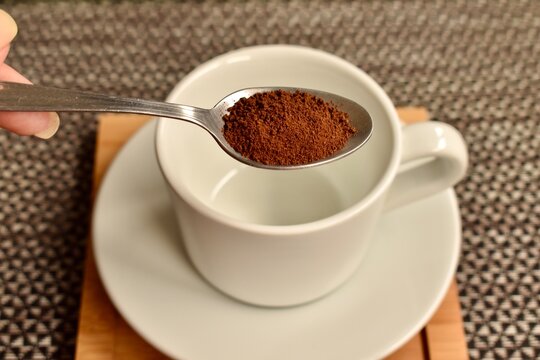 Tea spoon with instant coffee above a mug &mdash; quick and familiar coffee-making process.
