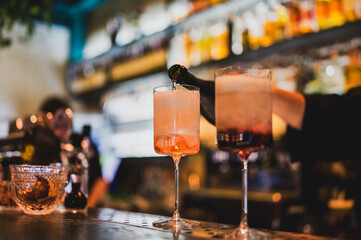 Bartender pouring cocktail into elegant glass at vibrant bar. Gradient drinks, blurred background, and warm lighting create a lively nightlife atmosphere