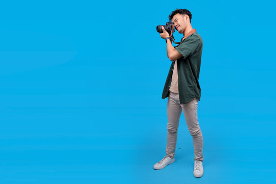Smiling Young Male Photographer Taking A Photo With His Digital Camera Isolated On Blue Background