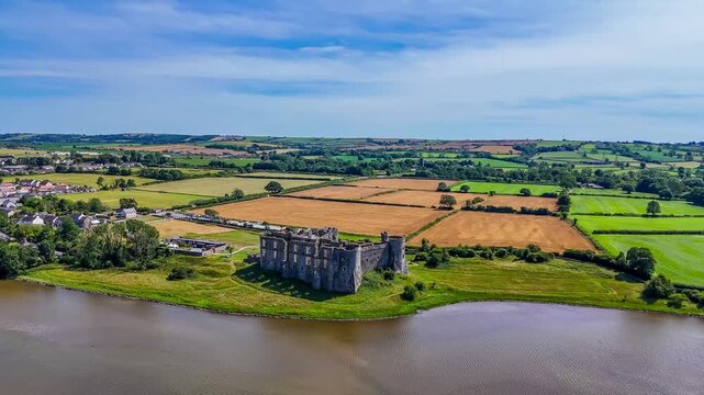 A distant rotating aerial view around the Castle ruins at Carew, South Wales in summertime