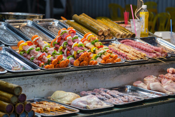 Colorful raw meat and vegetable skewers at a street food market. Raw meat and vegetable skewers displayed on trays at a vibrant street food market. Fresh ingredients ready for grilling