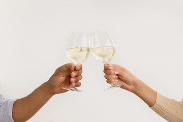 Covid-19, dinner, date and celebration anniversary and birthday at home. Hands of millennial african american male and female clink glasses with white wine on light background, empty space, cropped