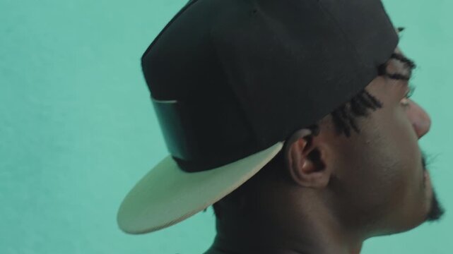 Close up side profile of young man in backward cap passing teal wall, focused gaze forward, subtle motion blur suggests movement, urban student vibe, minimal background