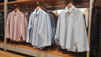 A selection of button-up shirts in soft pink, solid light blue, and striped white are neatly displayed on wooden hangers, offering classic wardrobe essentials in a store