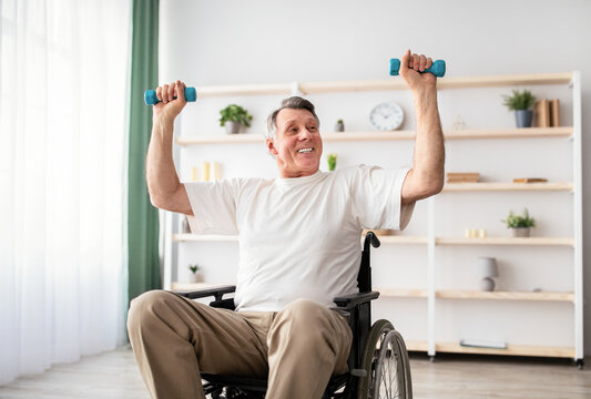 Physical activities for disabled elderly adults. Happy handicapped man in wheelchair making rehabilitation exerises with dumbbells at home. Positive impaired male working out indoors - Powered by Adobe