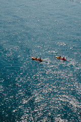 Two colorful kayaks with paddlers cross the glittering sea, surrounded by sparkling reflections under bright summer sunlight.