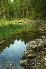Clear mountain lake with visible rocky bottom and tree reflections in Bavaria, Germany. Tranquil alpine water with natural details.