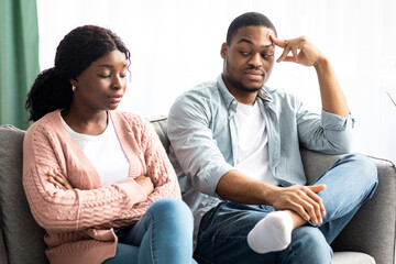Frustrated black woman sitting apart from her pensive boyfriend, young african american couple having fight at home, suffering from difficulties in relationships during coronavirus self-isolation