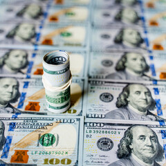 Fototapeta premium a lot of money banknotes in denominations of one hundred 100 American dollars lie on the table evenly laid out, on top stands a roll of money dollars tied with a rubber band, background with money Ame
