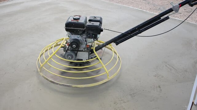 Construction worker using power trowel on concrete surface, Close-up of a construction worker operating a power trowel machine to smooth and finish freshly poured concrete on a building site.