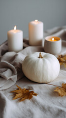 Naklejka premium White pumpkin with autumn leaves and glowing candles on soft fabric creating a warm and cozy seasonal still life atmosphere. 