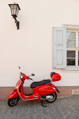 Red scooter parked by a white wall with window and lantern, urban street scene © Yevhenii Rukavitsyn