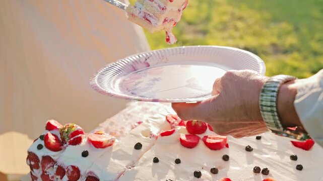 Close-up of hands sharing berry cake in sunlit outdoor wedding moment