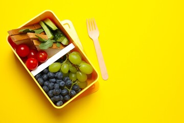 Tasty school snack with a lunchbox with fruits on a yellow background. Top view