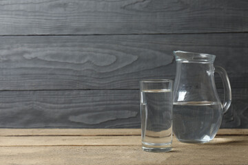 Glass of water with jug at wooden table, closeup. Drinking clear water in the morning for health. Space for text 