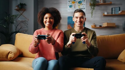 Young multi ethnic couple having fun playing video games sitting on a comfortable sofa in their modern living room, enjoying their leisure time together - Powered by Adobe