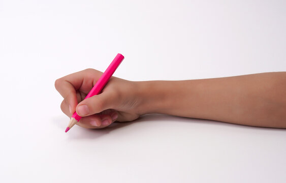 Childs hand holding a bright pink pencil, ready to write on a white background.