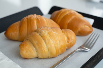 Three golden croissants topped with coarse sugar sit on parchment paper beside a fork.