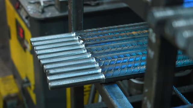 Thick metal reinforcement bars with rolled threads stacked in warehouse