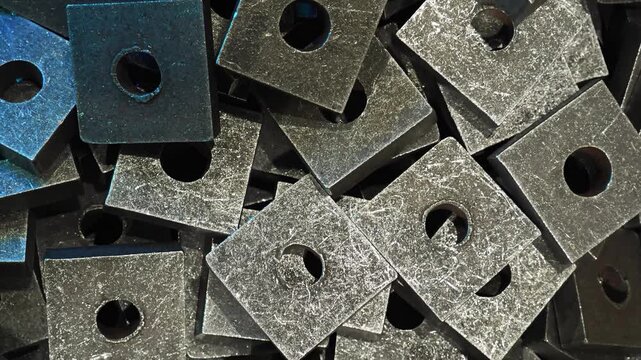 Thick square metal washers with central holes stacked in pile