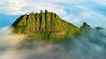 Admire the majestic Drangarnir Cliff towering over the landscape of the Faroe Islands. This natural wonder is enveloped in wispy clouds, showcasing the wild beauty of this remote destination.