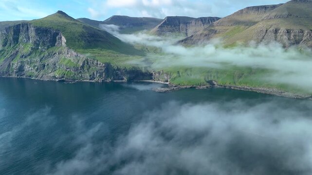 Majestic cliffs rise above the serene waters of the Faroe Islands. Rolling fog envelops the lush green landscape, creating an enchanting atmosphere. Natures artistry unfolds in every view.